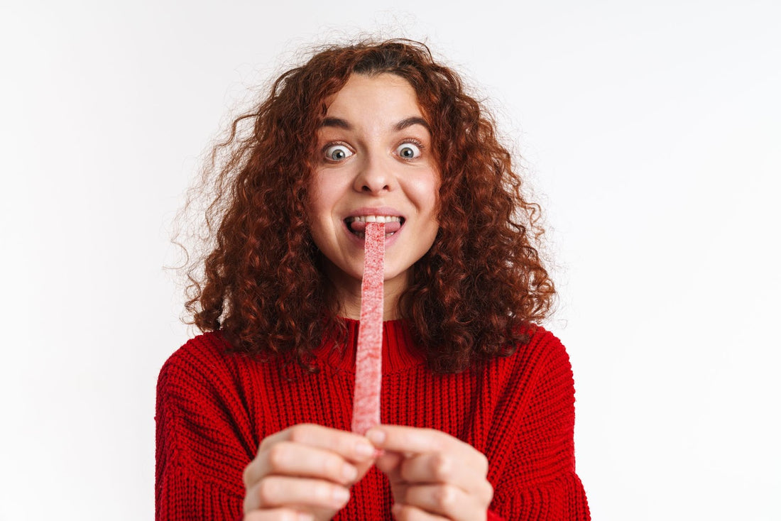 Curly-haired girl with ginger locks grimacing in delight during an extreme sour candy challenge