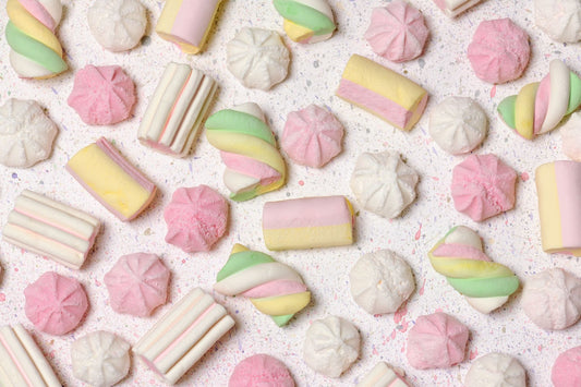 Assorted pastel-colored sweets, including meringue, taffy, and marshmallows, artfully arranged on a creative, abstract background.