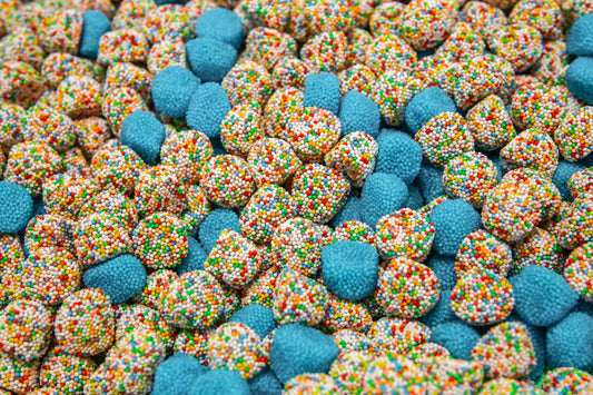 Multicolored gummy clusters with scattered candy nibs on a white table.