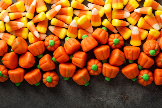 Colorful orange candy corns arranged on a plate with some spillovers and a decorative pumpkin on the side.