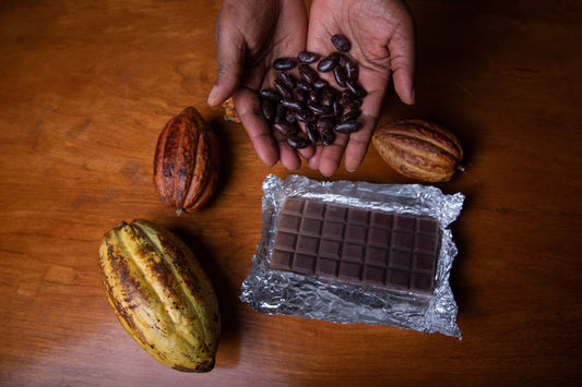 A farmer cradling cocoa beans in his palm, with ripe cocoa pods and a chocolate bar arrayed on a brown table 