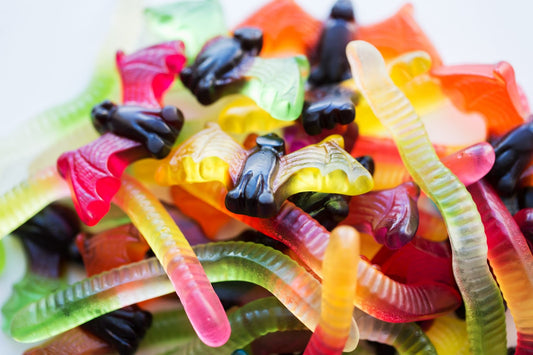 A heap of multicolored gummy worms and various other shaped candies fills the container, enticing it with its vibrant hues and sugary allure.