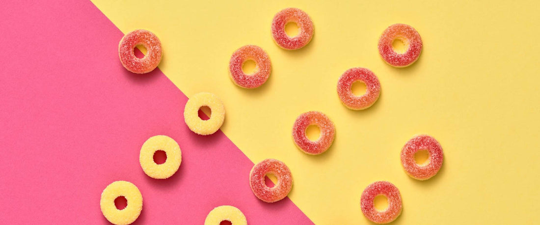 Several peach ring gummy candies rest on a backdrop that is half pink and half yellow.