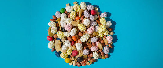 An assortment of nuts, dried fruits, and candies in a circular pile against a blue background. 