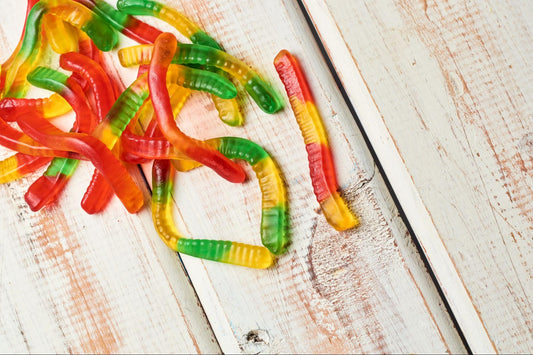 Some colorful neon gummy worms on a wooden table.