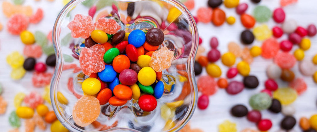 An image of assorted vibrant candies collected in a glass dish against a white background.